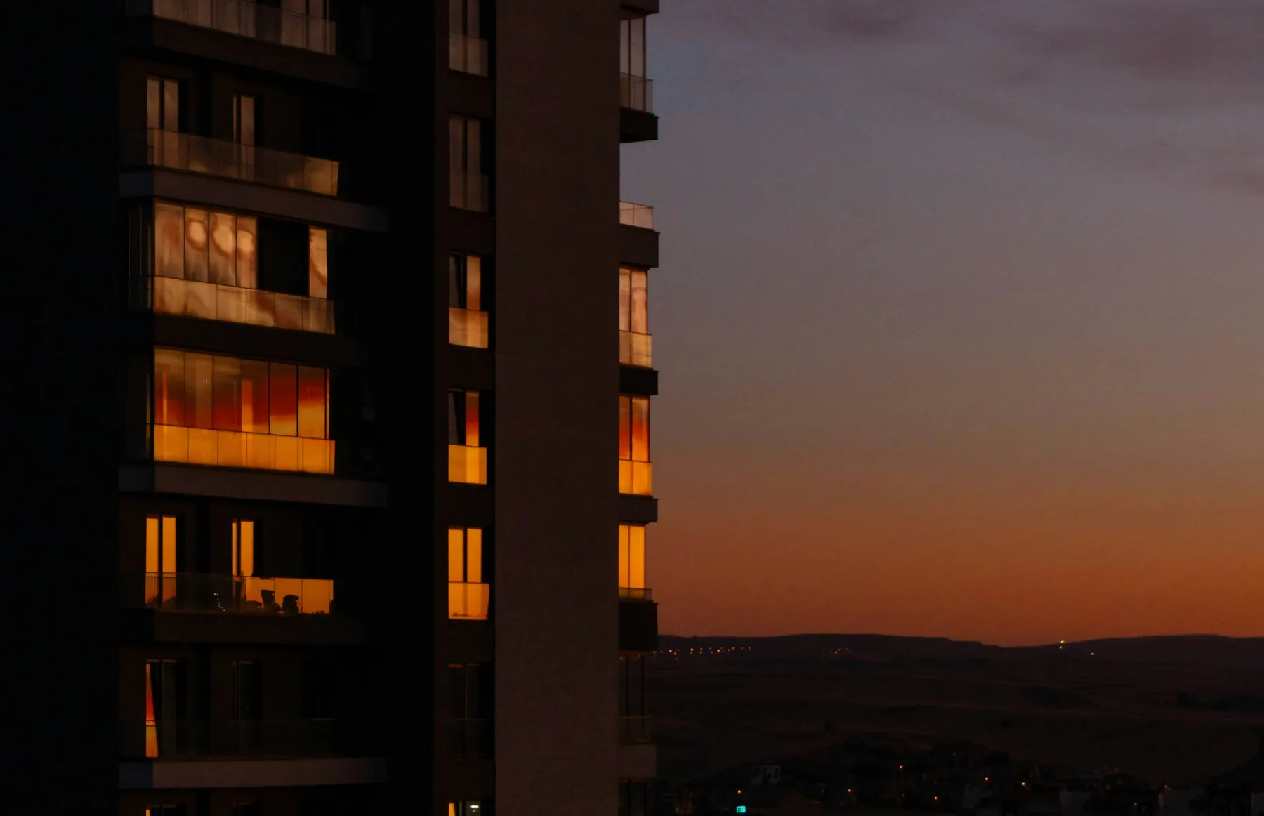 An apartment facade at dusk with the windows lit.